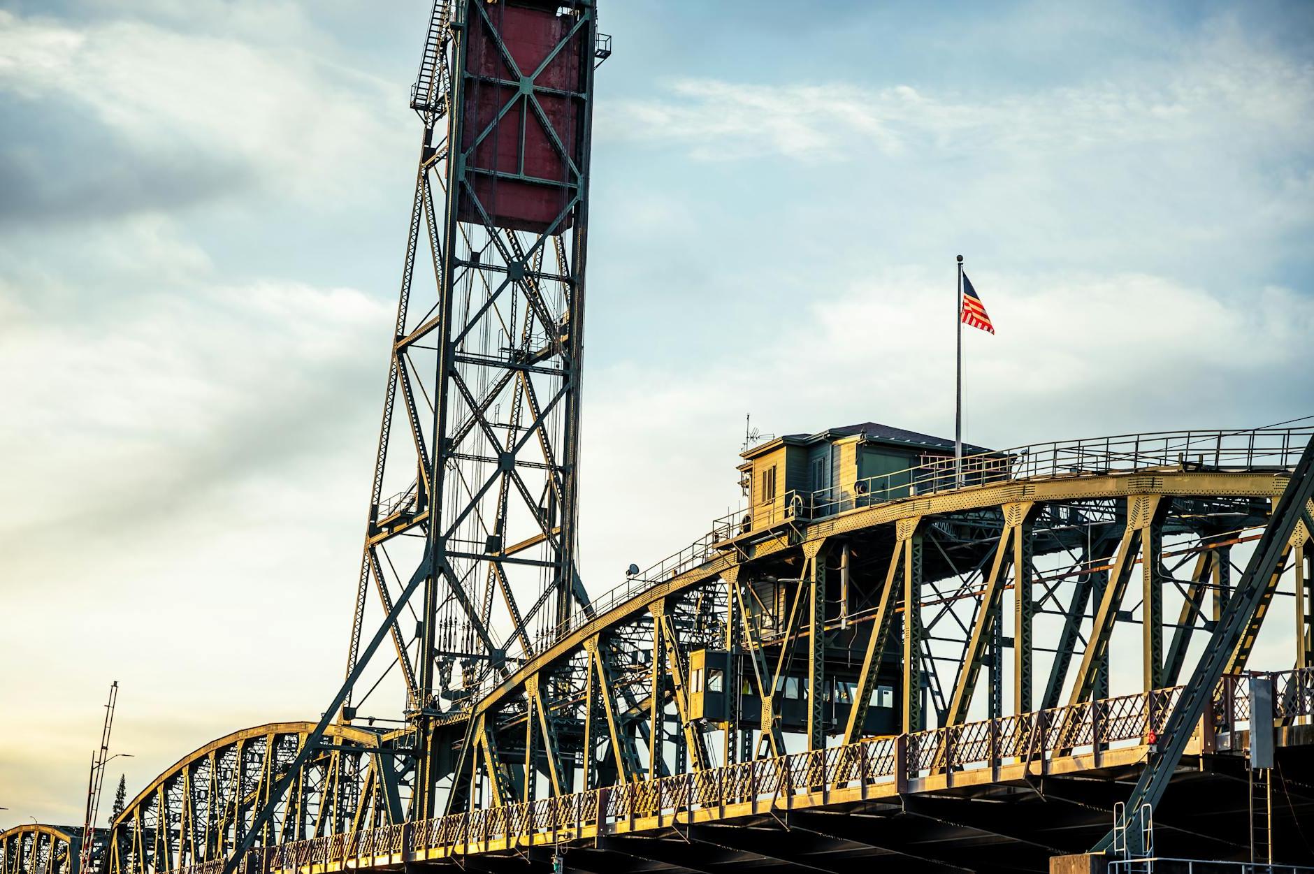 Low angle of metal Hawthorne Bridge with vertical lift and waving US flag against cloudy sunset sky in Portland