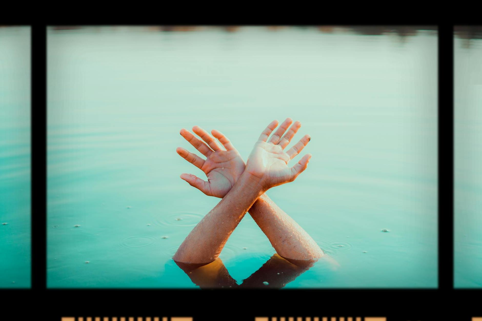 Film with photo of crop anonymous person raising hands in water in daytime