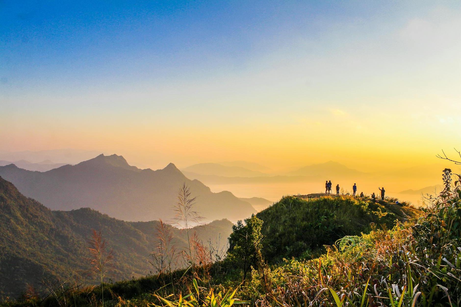 Photo of People Standing on Top of Mountain Near Grasses Facing Mountains during Golden Hours