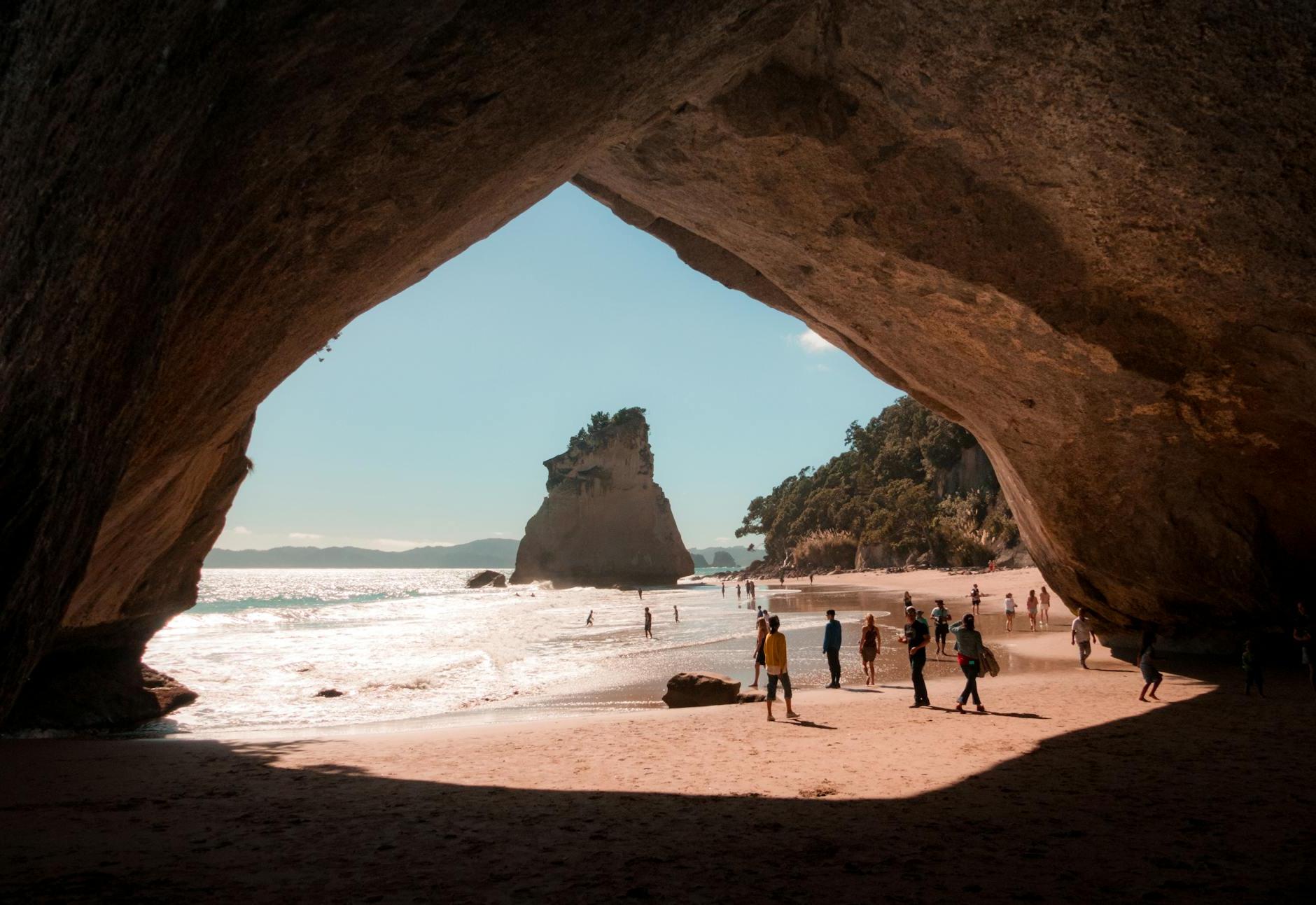 Person Walking Beside Cave and Body of Water